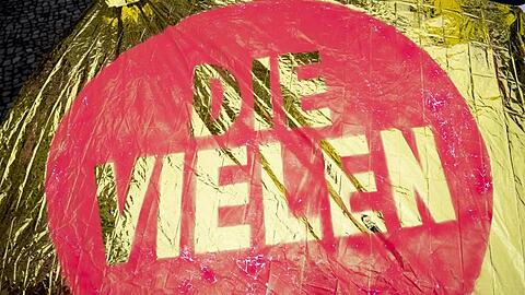 &bdquo;Die Vielen" steht auf einer glänzenden Fahne. Foto: Christoph Soeder/Archiv