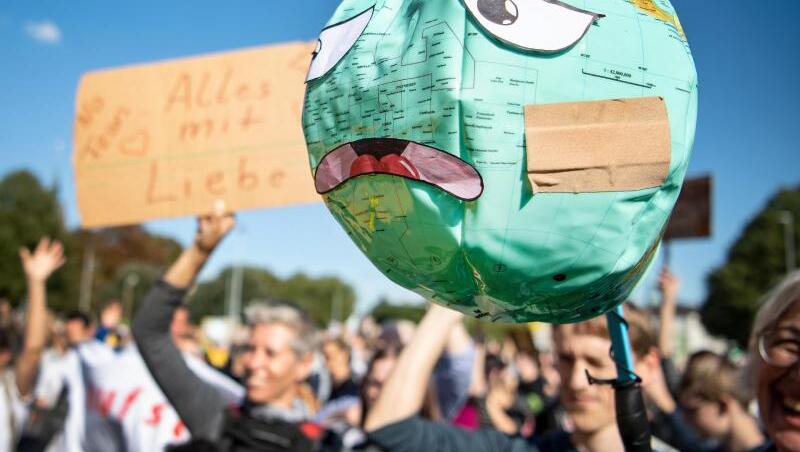 Demonstranten halten einen Luftballon mit Globusaufdruck hoch, der mit einem Pflaster und unglücklichen Gesichtszügen beklebt ist. Foto: Sina Schuldt/Archiv Demonstranten halten einen Luftballon mit Globusaufdruck hoch, der mit einem Pflaster und unglücklichen Gesichtszügen beklebt ist. Foto: Sina Schuldt/Archiv