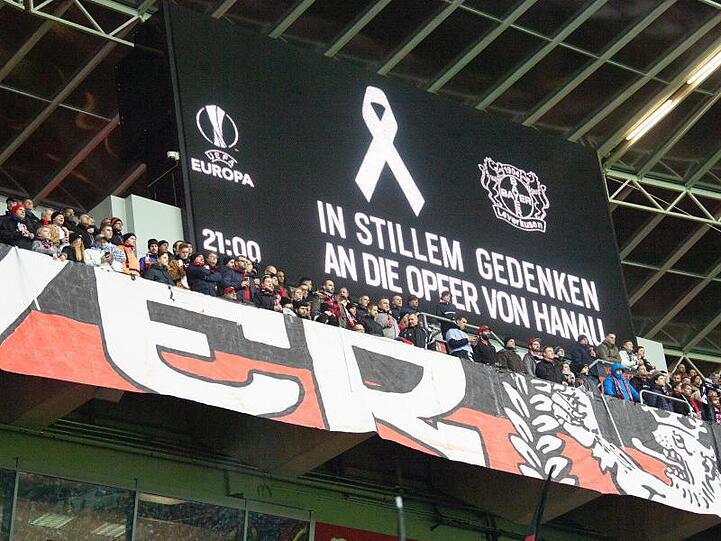 Fans stehen für eine Schweigeminute für die Opfer von Hanau auf der Tribüne.