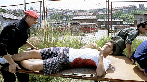 Sarajevo im Juni 1993: Ein Zivilist und ein Soldat tragen gemeinsam einen jungen Mann, der von einem Scharfschützen getroffen wurde auf einer Tür als Ersatztrage. Wie jetzt herauskam, sollen damals Privatpersonen Geld gezahlt haben, um auf Zivilisten zu schießen – darunter auch Deutsche.