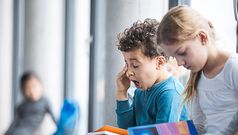 Ist die Lektüre vielleicht doch nicht so spannend? Ein junger Bub sitzt neben einem Mädchen und gähnt – während er ein geschlossenes Buch in den Händen hält. Ihnen soll die Verfassung näher gebracht werden.