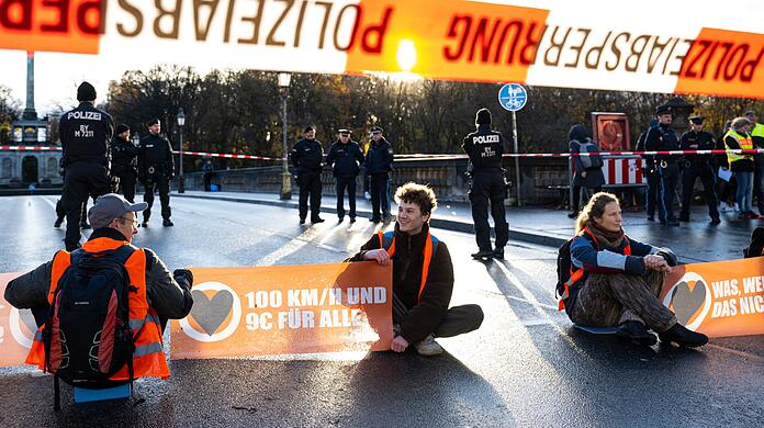 Aktivisten der Umweltschutzbewegung "Letzte Generation" blockieren auf einer Straße in München den Verkehr.