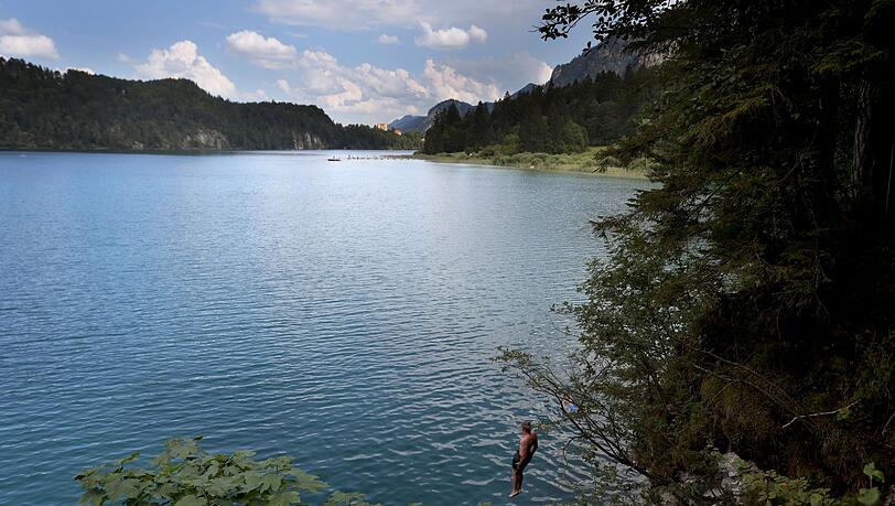 Ein junger Mann springt vom steilen Ufer in das türkisfarbene Wasser des Alpsees.
