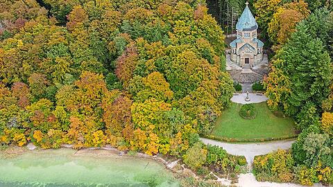 Die Votivkapelle zum Gedenken an den Kini in Berg, umgeben von Natur. Am Ufer davor ist das Kreuz für Ludwig II. zu erkennen.