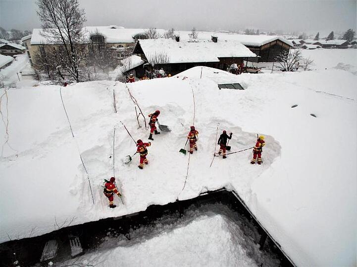 Helfer der DLRG Bayern räumen die Schneemassen von einem Hausdach.