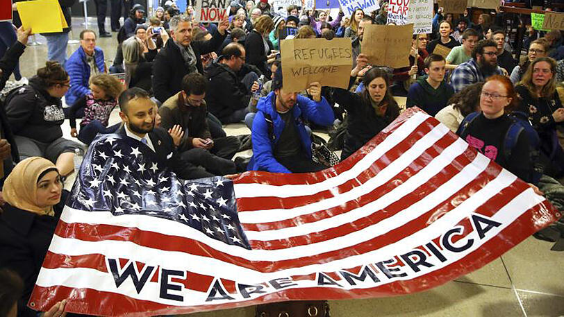 Demonstranten sitzen im Flughafen von Seattle auf dem Boden und halten ein Plakat mit der Aufschrift "Wir sind Amerika".