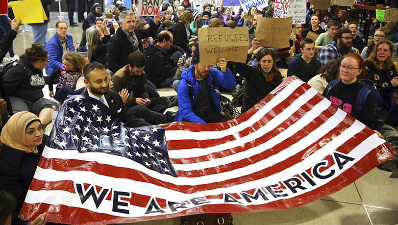 Demonstranten sitzen im Flughafen von Seattle auf dem Boden und halten ein Plakat mit der Aufschrift "Wir sind Amerika". Demonstranten sitzen im Flughafen von Seattle auf dem Boden und halten ein Plakat mit der Aufschrift "Wir sind Amerika".