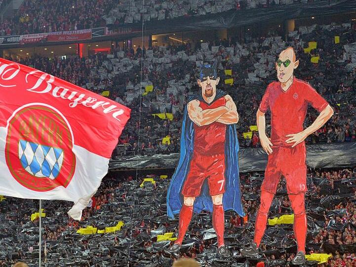 Franck Ribery als "Batman" (l) und Arjen Robben als "Robin" als überdimensionale Figuren vor dem Fanblock des FC Bayern München. Foto: Peter Kneffel/Archivbild