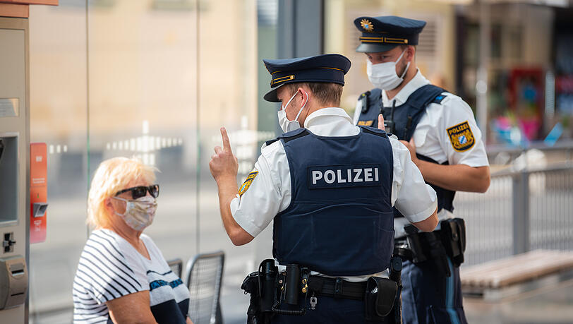 Zwei Polizisten nehmen an einer Tram-Haltestelle von einer Frau nach einem Verstoß gegen die Maskenpflicht im öffentlichen Nahverkehr die Personalien auf.