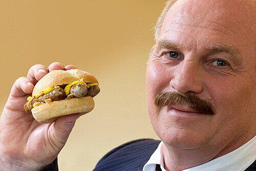 Mit angeklebtem Schnauzbart und im Film mit Baskenmütze wirbt Uli Hoeneß für seinen &bdquo;Nürnburger&ldquo; &ndash; drei Nürnberger Bratwürste im Weckla mit Zwiebel und Senf.