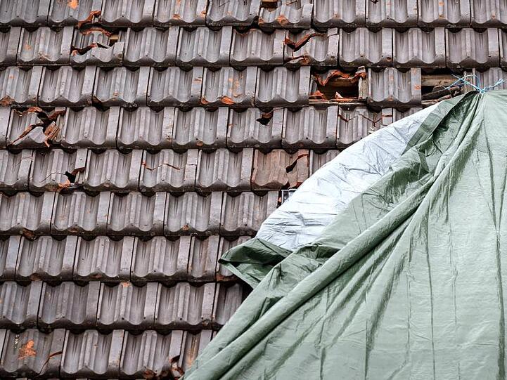 Ein vom Sturm und Hagelkörnern beschädigtes Dach nahe München ist zum Schutz mit einer Plane abgedeckt.