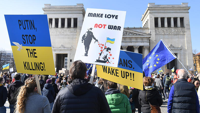 Teilnehmer einer Kundgebung gegen den Krieg in der Ukraine demonstrieren auf dem Königsplatz mit Tafeln mit der Aufschrift "Make Love - Not War" und "Putin stop the Killing!"