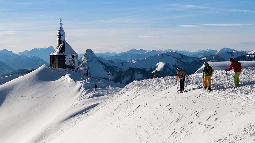 Skifahrer laufen zur Piste unterhalb der Wallberg-Kapelle.