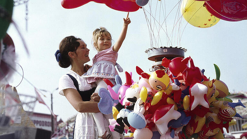Am Fr&uuml;hlingsfest in den 60er Jahren: Eine fr&ouml;hliche Mutter h&auml;lt ihre Tochter auf dem Arm, die einen Luftballon erhaschen m&ouml;chte. Ob sie einen bekommen hat?
