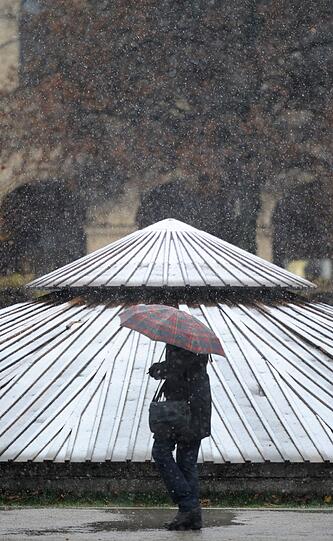 Schneeregen: Eine Spaziergängerin im Münchner Hofgarten hat sich den Schirm tief über den Kopf gezogen.
