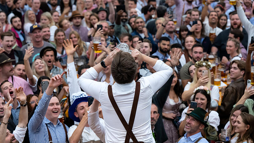 Ein Mann trinkt ein Bier und wird im Hofbräu-Zelt von der Menge angefeuert.