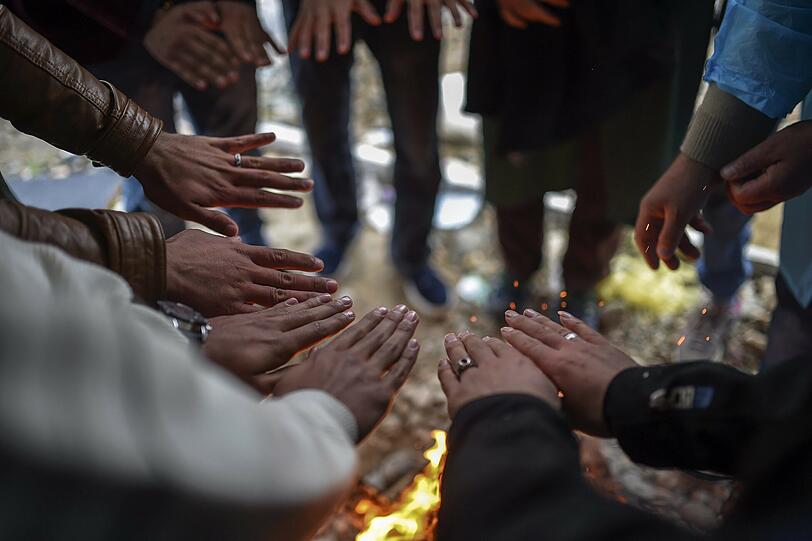 In Mazedonien wärmt sich eine Gruppe Flüchtlinge die Hände an einem Lagerfeuer.
