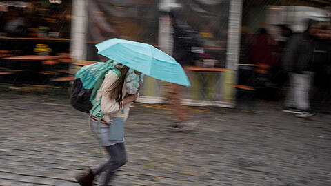 Eine Frau läuft bei einsetzendem Herbstregen mit ihrem Schirm über den Viktualienmarkt in der Münchner Innenstadt.
