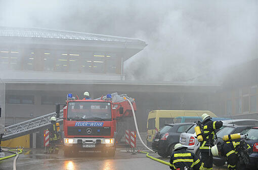 Feuerwehrmänner stehen in Titisee-Neustadt (Baden-Württemberg) vor einer brennenden Behindertenwerkstatt