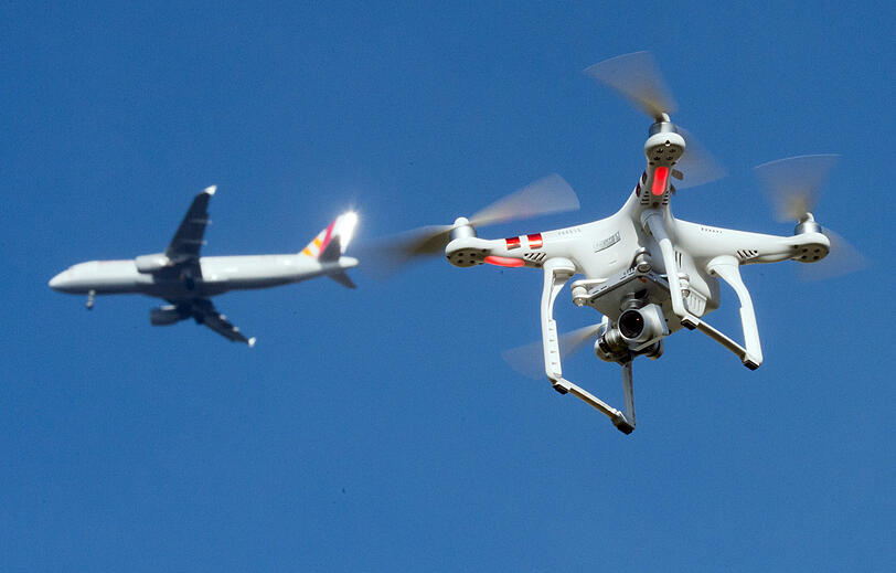 Eine private Drohne am himmel - daneben ist in einiger Entfernung ein Flugzeug im Anflug einen Flughafen.
