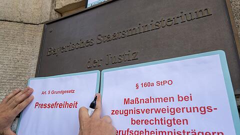 Ein Demonstrant befestigt Auszüge von Gesetzestexten am Eingang zum Justizministerium in München.