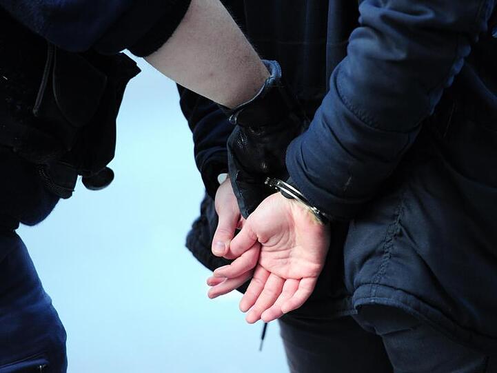 Ein Polizist führt einen mit Handschellen gefesselten Mann ab. Foto: Daniel Reinhardt/dpa/Archivbild