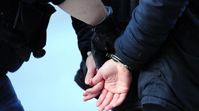 Ein Polizist führt einen mit Handschellen gefesselten Mann ab. (Symbolfoto)
