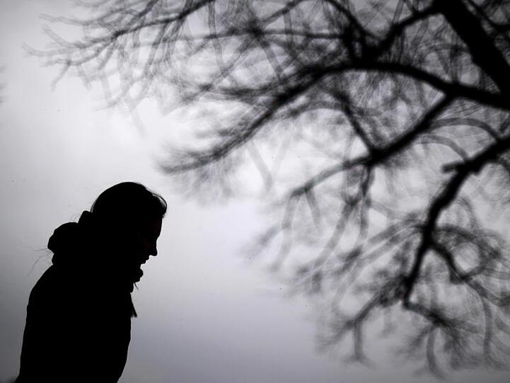 Dunke Silhouette eines Menschen ist neben einem kahlen Baum zu sehen. Foto: Julian Stratenschulte/Archivbild