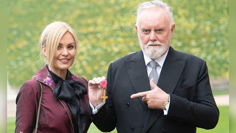 Queen-Drummer Roger Taylor mit seiner Ehefrau bei der OBE-Verleihung auf Schloss Windsor.