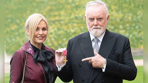Queen-Drummer Roger Taylor mit seiner Ehefrau bei der OBE-Verleihung auf Schloss Windsor.