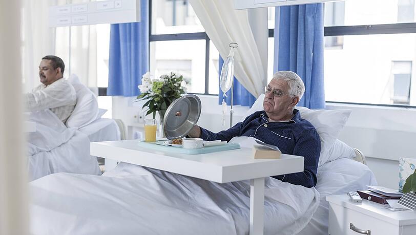 Skeptisch beäugt dieser Patient das, was sich unter der Warmhaltehaube verbirgt. Am Essen in Krankenhäusern, auch in München, wird oft gespart. Skeptisch beäugt dieser Patient das, was sich unter der Warmhaltehaube verbirgt. Am Essen in Krankenhäusern, auch in München, wird oft gespart.