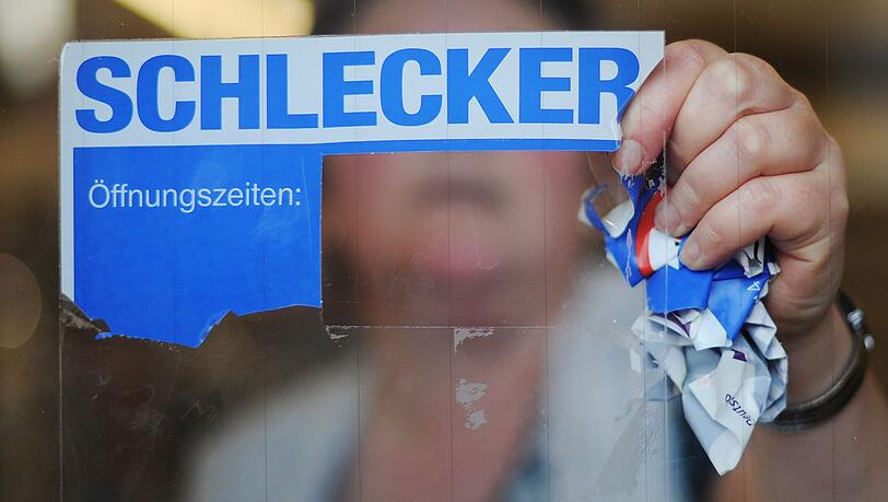 Eine Mitarbeiterin der Drogeriemarktkette Schlecker reißt im März 2012 das Firmenlogo von der Eingangstür einer Filiale.