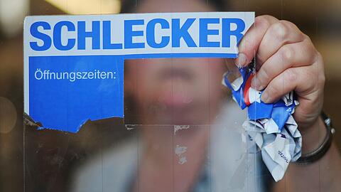 Eine Mitarbeiterin der Drogeriemarktkette Schlecker reißt im März 2012 das Firmenlogo von der Eingangstür einer Filiale.