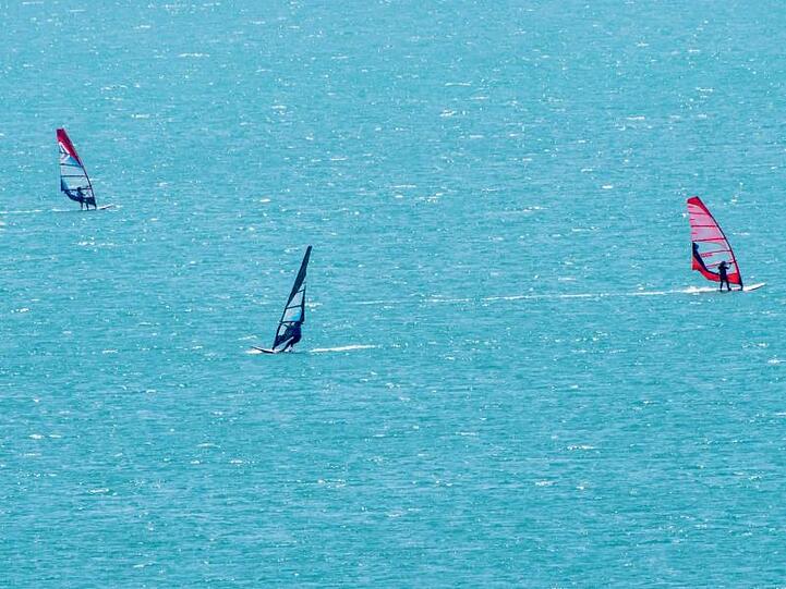 Windsurfer nutzen die guten Winde für eine Runde auf dem Walchensee in Oberbayern.