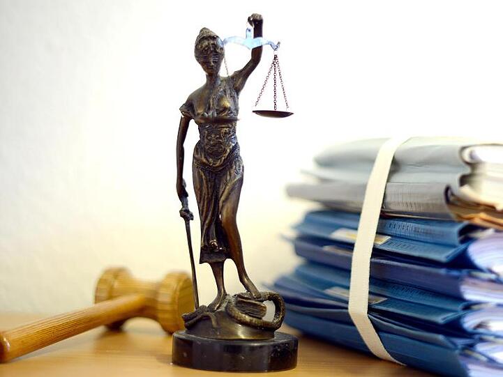 Eine Statue der Justitia steht neben Aktenbergen. Foto: Volker Hartmann/dpa/Archivbild