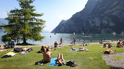 Touristen und Einheimische nehmen am Strand von Riva del Garda ein Sonnenbad. Der Ort l&auml;sst sich auch mit dem Zug erreichen.