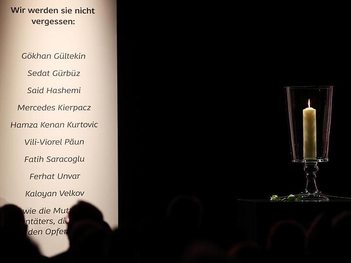 Eine Kerze steht neben den Namen der Opfer bei der Gedenkfeier für die Opfer von Hanau.