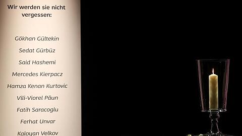 Eine Kerze steht neben den Namen der Opfer bei der Gedenkfeier für die Opfer von Hanau.