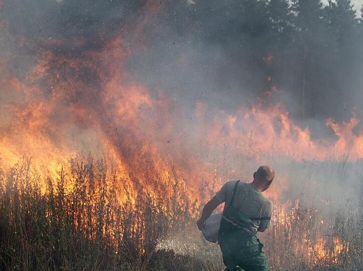 Mit Wasser aus einer großen Schüssel versucht ein Helfer, meterhohe Feuerwalzen zu löschen.