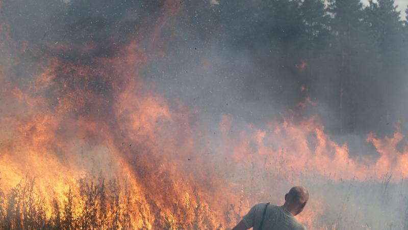 Mit Wasser aus einer großen Schüssel versucht ein Helfer, meterhohe Feuerwalzen zu löschen. Mit Wasser aus einer großen Schüssel versucht ein Helfer, meterhohe Feuerwalzen zu löschen.