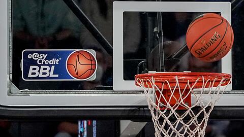 Ein Ball fliegt auf den Korb zu, an dem ein Logo der Basketball-Bundesliga klebt.