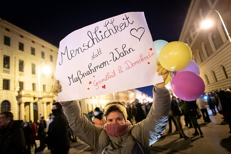 Eine Versammlungsteilnehmerin hält bei einer Demonstration der Querdenken-Bewegung vor dem Bayerischer Verwaltungsgerichtshof ein Schild mit der Aufschrift "Menschlichkeit statt Maßnahmen-Wahn, - Gesundheit & Demokratie" in den Händen.