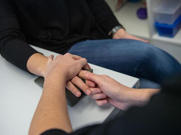 Eine Ergotherapeutin massiert einer Frau während einer Handtherapie einen Finger.