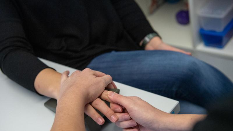 Eine Ergotherapeutin massiert einer Frau während einer Handtherapie einen Finger. Eine Ergotherapeutin massiert einer Frau während einer Handtherapie einen Finger.