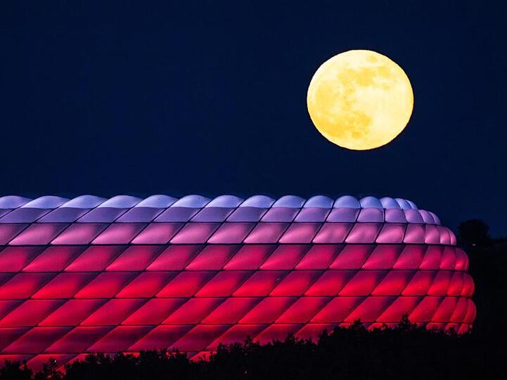 Der Vollmond geht hinter der beleuchteten Allianz-Arena auf. Foto: Peter Kneffel/dpa/Archivbild