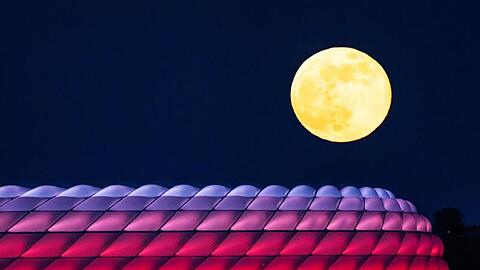 Der Vollmond geht hinter der beleuchteten Allianz-Arena auf. Foto: Peter Kneffel/dpa/Archivbild