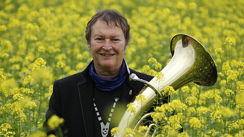 Hans-Jürgen Buchner mit einem Tenorhorn im Rapsfeld. Außerdem spielt er noch Trompete, Gitarre und Klavier.