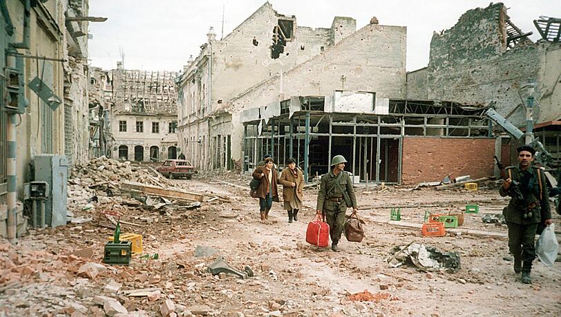 Das Archivbild zeigt Menschen, die am 19.11.1991 einen zerstörten Straßenzug in der Stadt Vukovar entlang gehen. In der Ausstellung zeigen Künstler einen Blick auf ihre Kindheit in Jugoslawien. Das Archivbild zeigt Menschen, die am 19.11.1991 einen zerstörten Straßenzug in der Stadt Vukovar entlang gehen. In der Ausstellung zeigen Künstler einen Blick auf ihre Kindheit in Jugoslawien.