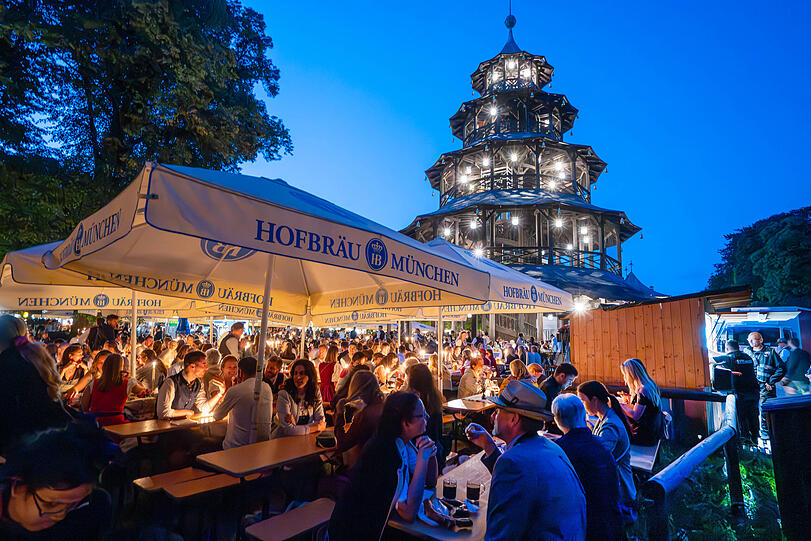 Viele Frühaufsteher in der Stadt: Schon in den frühsten Morgenstunden sitzen Besucher im Biergarten am Chinesischen Turm und bereiten sich auf den Kocherlball vor. Sie unterhalten sich, trinken Bier und essen ihre Brotzeiten.