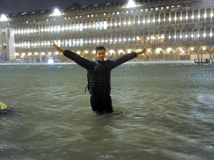 Ein Mann steht im Hochwasser auf dem überschwemmten Markusplatz.